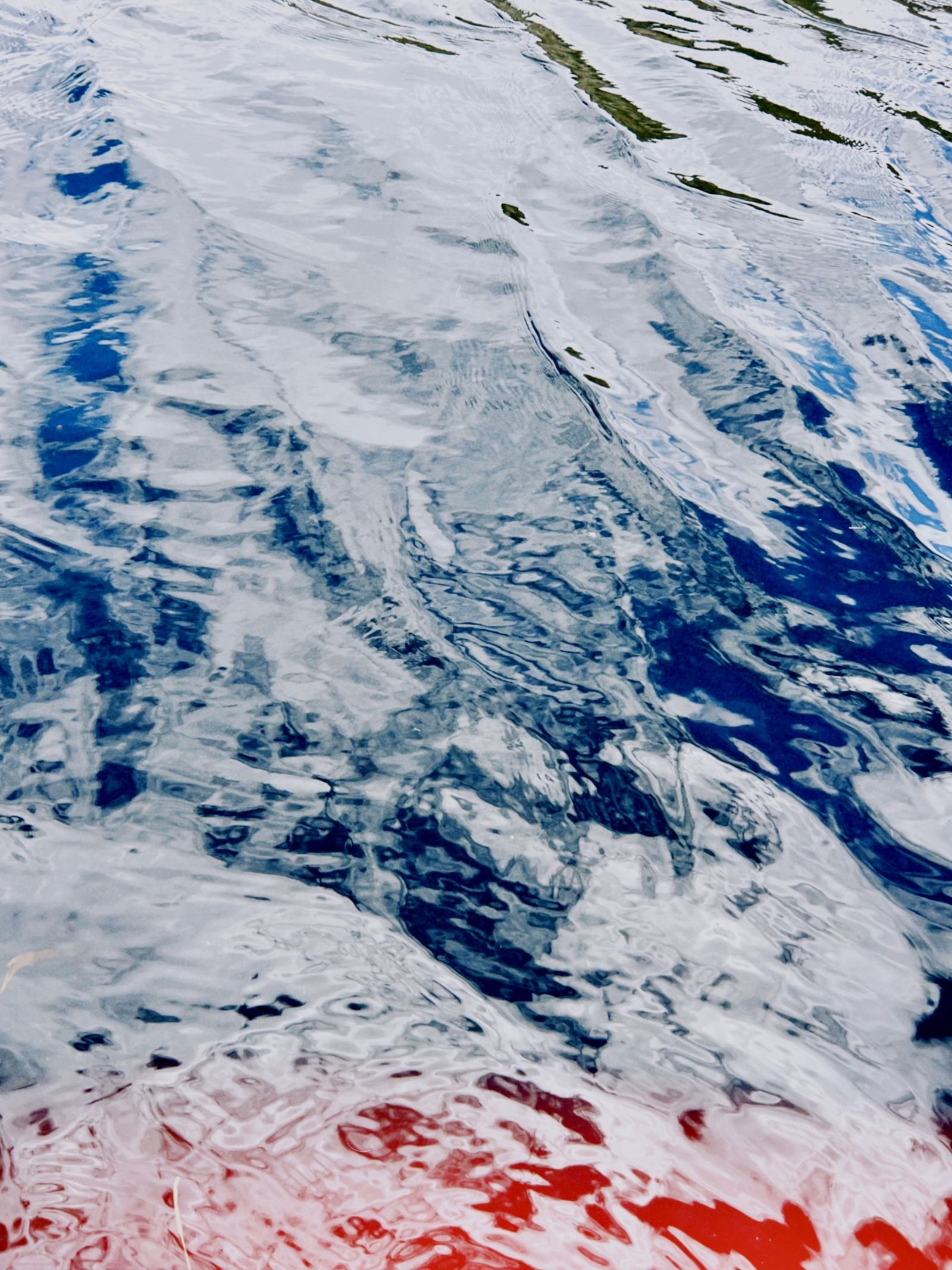 Ondulaciones del agua que descomponen reflejos azules, blancos y rojos