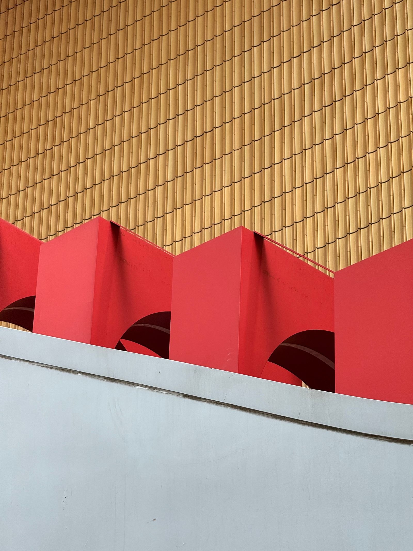 Arcos rojos y planos geométricos sobre una fachada de tonos dorados