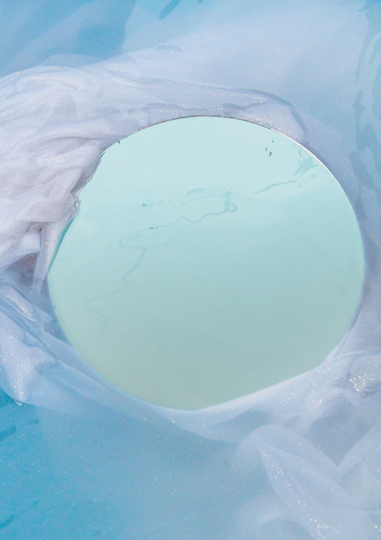 Un espejo circular entre reflejos de agua azul y luz suave